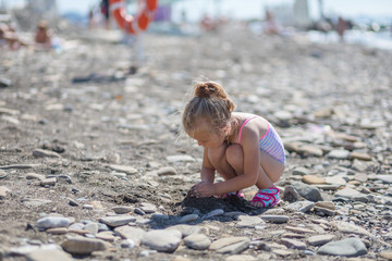 Cute baby girl playing with pebbles on the beach
