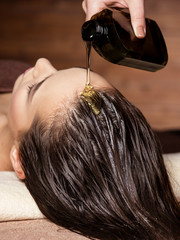 Cosmetologist pours balm for hair on head of  woman. Spa treatments.