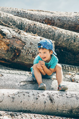 Preschool boy in a baseball cap sits on a log and laughs merrily