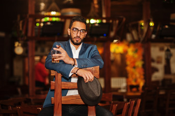 Handsome well-dressed arabian man with glass of whiskey and cigar posed at pub.