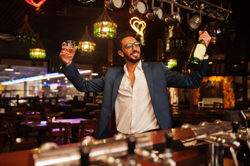 Handsome well-dressed arabian man with glass of whiskey and cigar posed at pub.