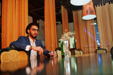 Handsome well-dressed arabian man with glass of whiskey and cigar posed at pub.