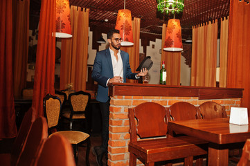 Handsome well-dressed arabian man with glass of whiskey and cigar posed at pub.