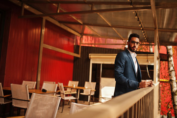 Fototapeta premium Handsome well-dressed arabian man smoke cigar with glass of whiskey at balcony of pub.