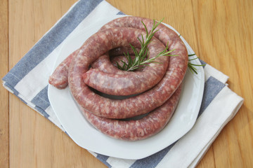 Raw italian long pork sausage with fresh rosemary branch on a plate on wooden table. Pork sausage...