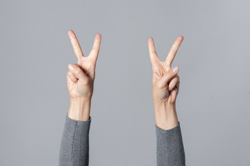 Woman showing victory gesture by her hands isolated on gray background.