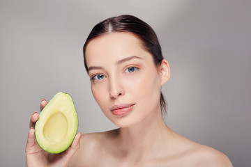 pensive tender calm brown-haired nude lady looking streight with perfect pure shine skin with avocado in the right hand