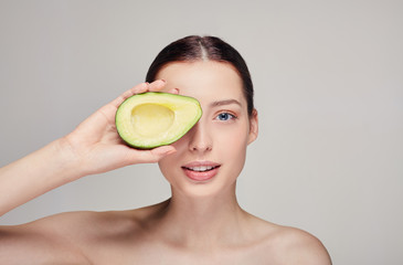 attractive tender brown-haired nude lady with perfect pure shine skin beautiful smile and avocado in right hand near eye