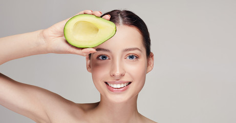 cheerful and happy brown-haired nude lady with perfect pure shine skin beautiful smile and avocado on top in hand near the forehead