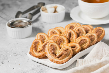 Puff pastry with sugar and cinnamon in a white ceramic plate on a light gray table