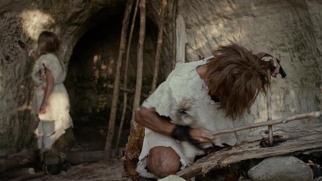 Primeval Caveman Wearing Animal Skin Trying to make a Fire with Bow Drill Method. Neanderthal Kindle First Man-Made fire in the Human Civilization History. Making Fire for Cooking. Zoom In Shot