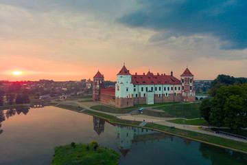 Obraz premium Mirsky Castle and its reflection in the lake in summer. Sunset in cloudy weather with rain clouds.