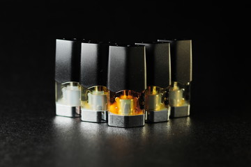 e-juice vape refill pods with liquids of different shades of orange yellow, black background isolated close up