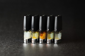 e-juice vape refill pods with liquids of different shades of orange yellow, black background isolated close up