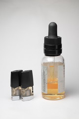 e-juice vape refill pods with with a bottle of orange e-liquid, isolated close up white background