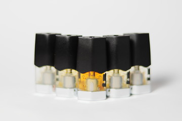 e-juice vape refill pods with liquids of different shades of orange yellow, white background shallow focus