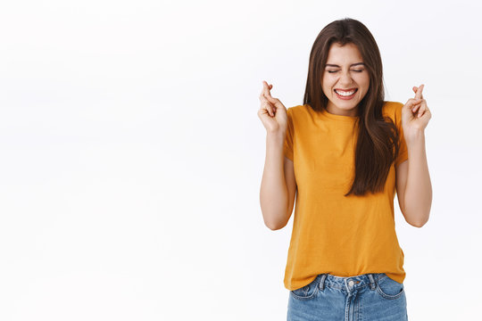 Dreamy, optimistic, hopeful excited girl believe she will win, have luck her side, cross fingers and close eyes, smiling, praying for dream come true, wishing, standing white background in temptation