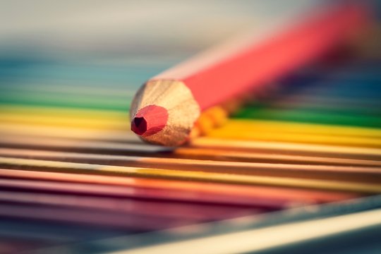 A portrait of a red colored pencil lying on top of other colorful pencils in their box.
