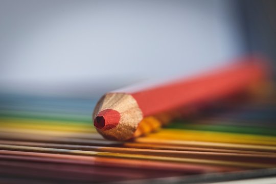 A Colorful Portrait Of A Red Colored Pencil Lying On Top Of Other Different Colored Pencils In Their Box.