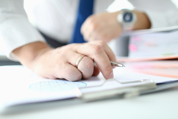 Focus on male hand with golden wedding ring holding ball pen. Man in office reading conditions of profitable contract. Business concept. Blurred background