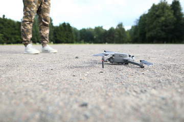 Focus on modern grey copter on ground. Man in khaki trousers controlling it. Professional drone with camera preparing to start. Take off for monitoring private property or military object