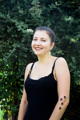 Young beautiful girl in black dress with tattoo on her hand in the park 