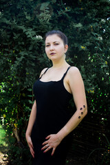 Young beautiful girl in black dress with tattoo on her hand in the park 