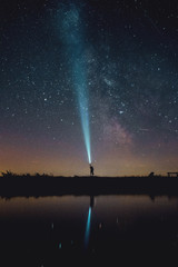 A adventure hiker person in the mountains holding a torch ray into the night sky with the milky way...