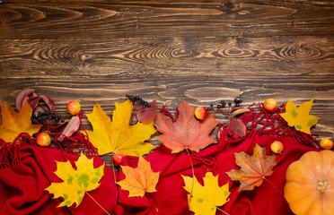 Autumn composition of yellow leaves, pumpkin, a red scarf and apples on a wooden background. Top view, flat lay.