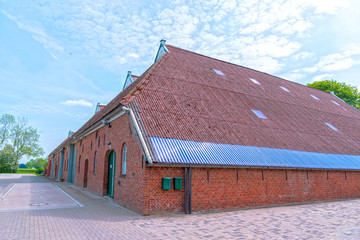 Old Dutch barn at a farm of red brick and red roof tiles. Round barn doors.