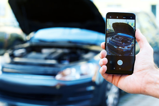 Closeup male hand is holding smartphone with picture of auto with open hood. Mechanic repairman is making photo of automobile engine motor. Software for car diagnostics and maintenance concept.