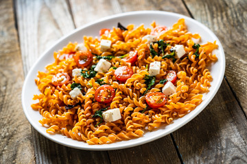 Pasta with tomatoes and white cheese on wooden table