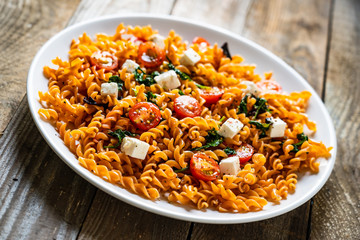 Pasta with tomatoes and white cheese on wooden table
