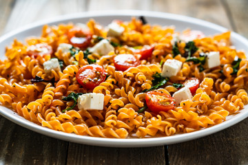 Pasta with tomatoes and white cheese on wooden table