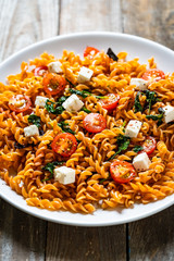 Pasta with tomatoes and white cheese on wooden table