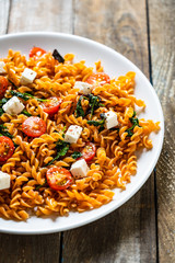 Pasta with tomatoes and white cheese on wooden table