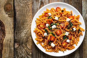 Pasta with tomatoes and white cheese on wooden table