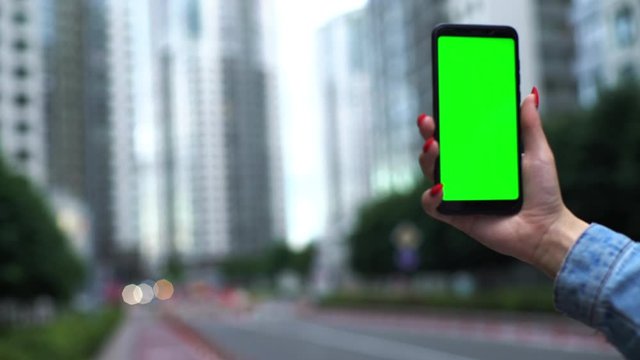 Woman use of smart phone with green screen, chroma key modern city skycrapers background