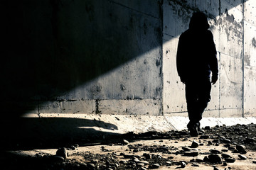 A man going out of an abandoned tunnel leaving a strong shadow behind. Man going to light.