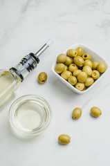 Green olives in a white ceramic bowl and glass bottle of olive oil on a white background. Top view.