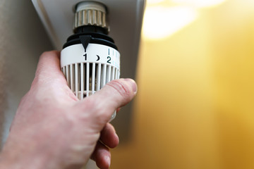Hand of man adjusting radiator thermostat valve to number 1 icon, symbol for saving money at...