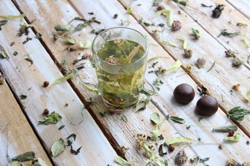 Obraz na płótnie Canvas Glass with herbal tea on wooden background with dry herbs an chocolate sweets