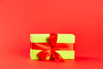 Christmas composition. Green gift box with a red ribbon on a red background. Side view. a Christmas gift