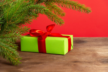 Christmas composition. Green gift box under the Christmas tree on a wooden table near a red background. a Christmas gift