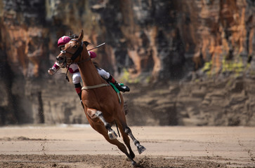 Galloping race horse and jockey in action,  horse racing on the beach with coastal cliffs in...