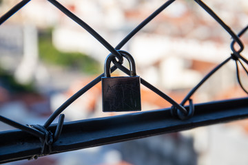 Detail of padlocks placed on the security fence of the Santa Just lift in Lisbon with the city landscape in the background