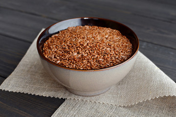 flax seeds in bowl with linen fabric on wooden background