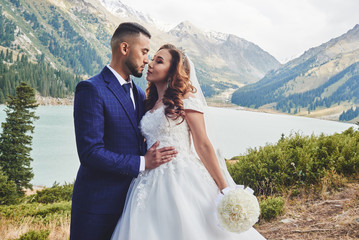 Beautiful wedding photo on mountain lake. Happy Asian couple in love, bride in white dress and...
