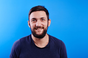 Portrait of toothy smiling and joyfully laughing handsome caucasian brutal bearded man dressed in casual isolated on blue background