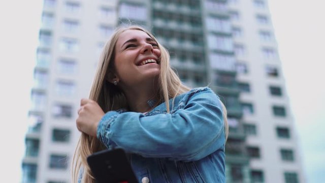 concept portrait of young millenial attractive happy emotional girl Cheerful female tourist using her modern telephone device laughing on streets in urban setting. positive traveller strolling and